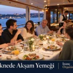 Teknede akşam yemeği için çiçeklerle süslenmiş masada sohbet eden konuklar.